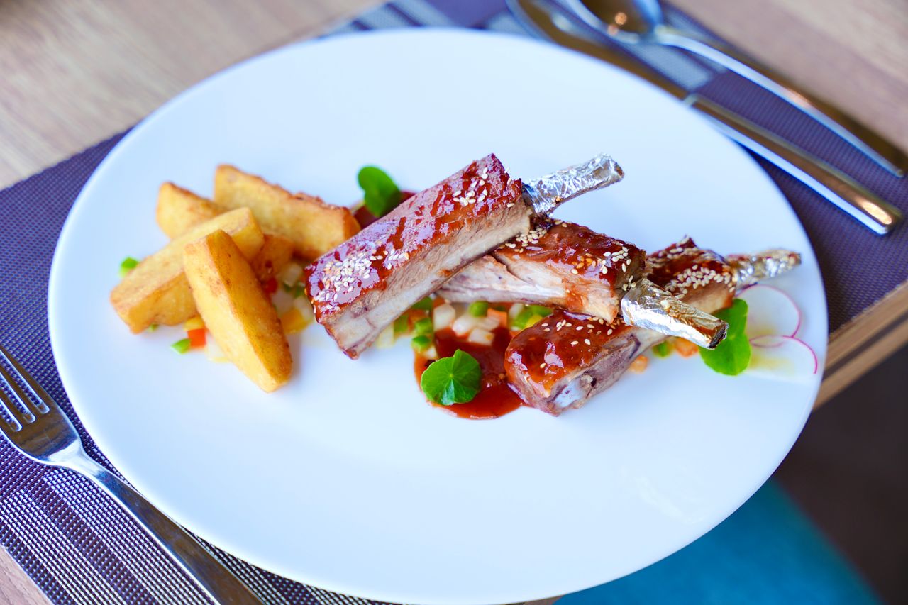 Close-up of gourmet BBQ spare ribs served with potato wedges and vegetables on a white plate.