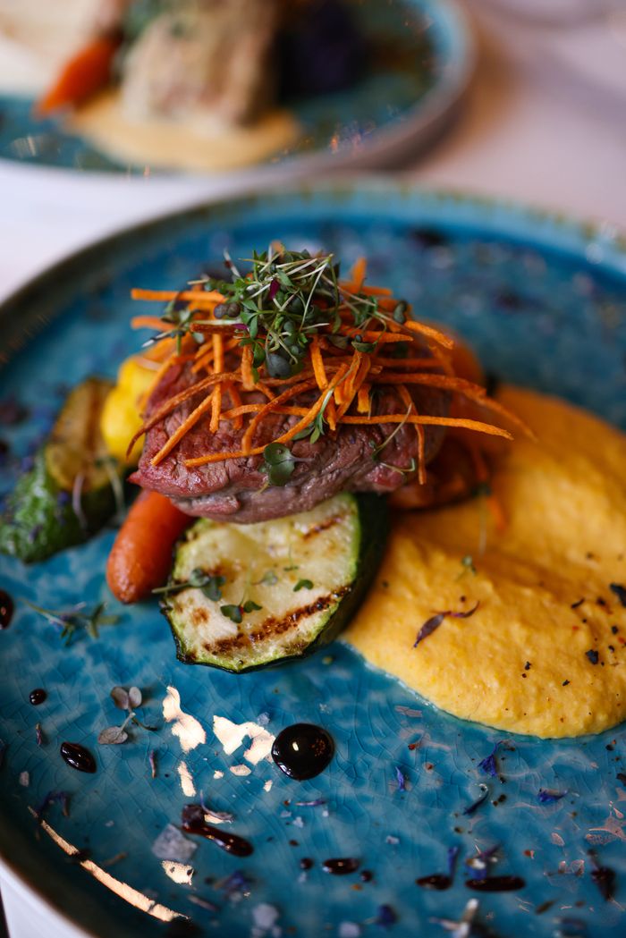 A sophisticated gourmet meal featuring grilled steak, vegetables, and puree on a blue plate.